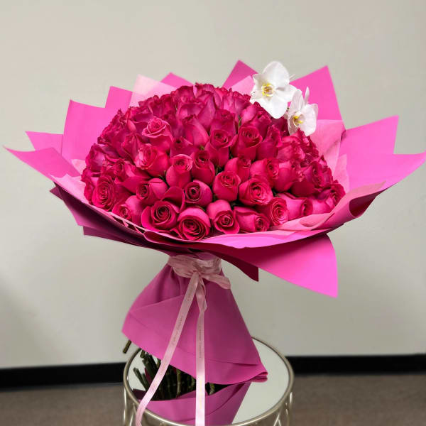 Large bouquet of hot pink roses with white orchids wrapped in bright pink paper