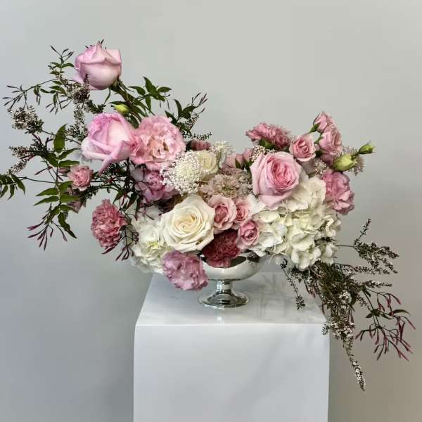 Low pink and white rose and hydrangea arrangement in a silver pedestal bowl with airy trailing branches.