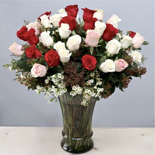 Tall vase of red, white, and pale pink roses with small white filler flowers.