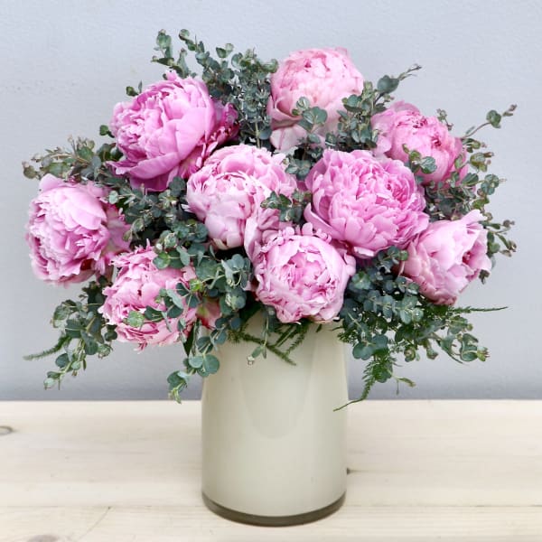 Pink peonies arranged in a white vase with eucalyptus