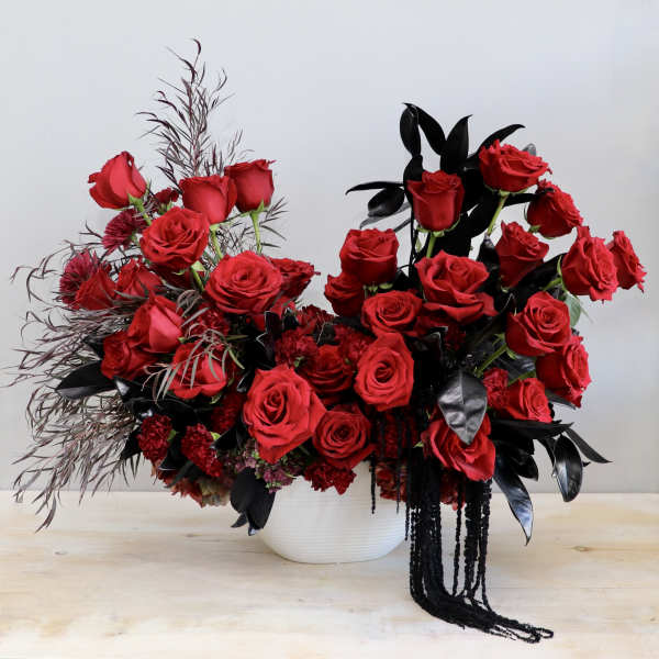 Asymmetrical arrangement of red roses with red carnations and black foliage in a white bowl vase