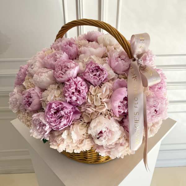 Pink peonies in a wicker basket with a ribbon bow