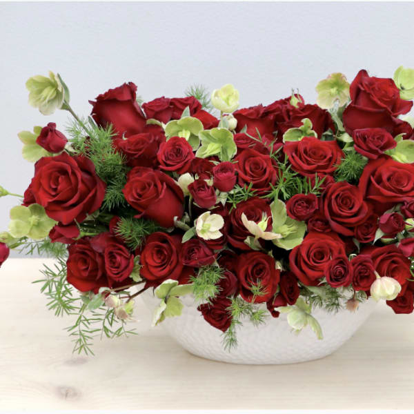 Red roses and pale green flowers in a white bowl vase