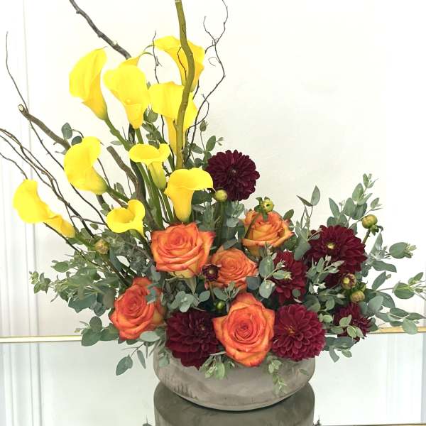 Arrangement of yellow calla lilies, orange roses, and burgundy dahlias in a low vase