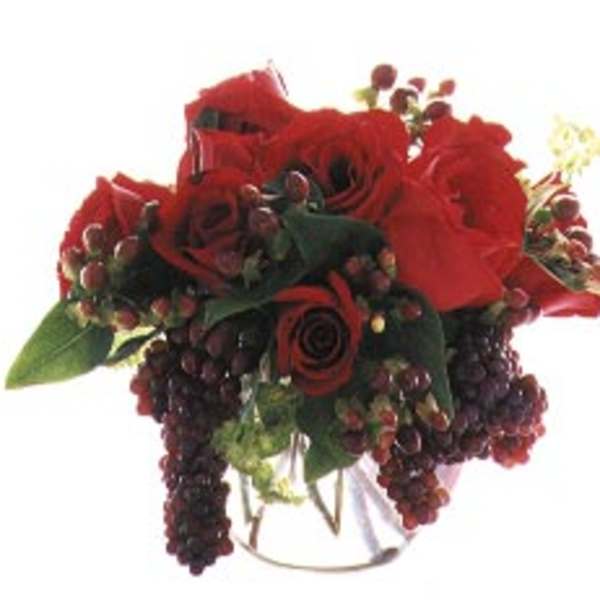 Red rose bouquet with dark berry accents in a clear vase