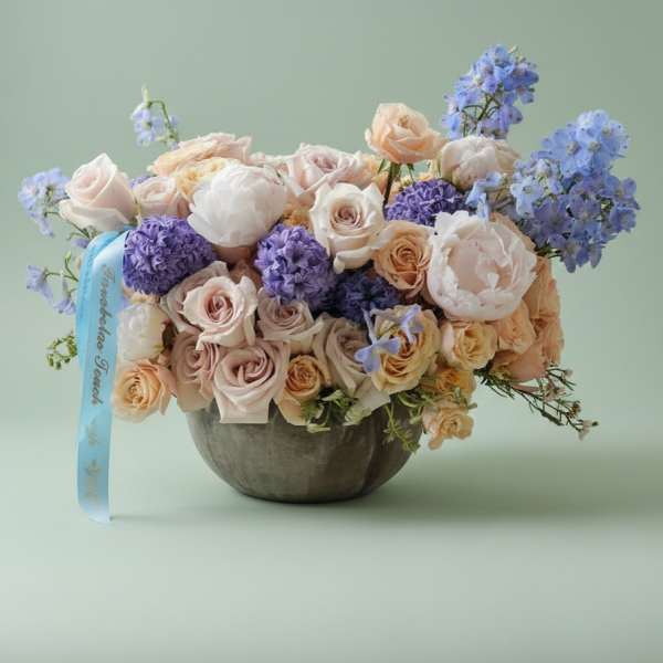 Pastel rose bouquet in a round vase with a blue ribbon