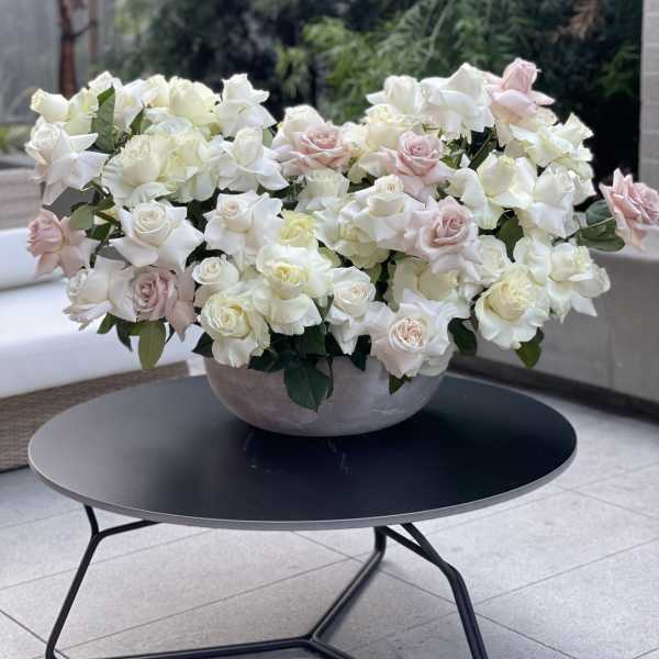 Large bowl arrangement of white and blush roses on a table
