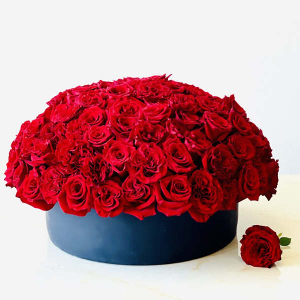 Round box arrangement of red roses with one loose rose beside it
