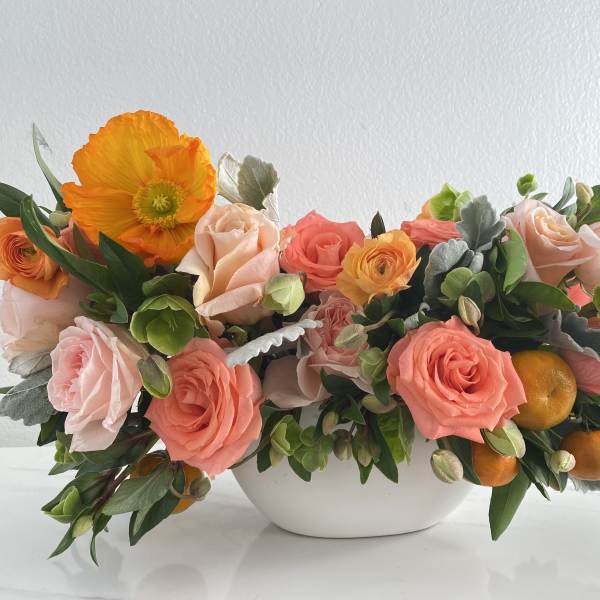 Coral and peach roses with orange poppies in a white bowl vase