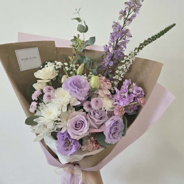 Hand-tied bouquet of lavender, white, and pink flowers wrapped in brown paper