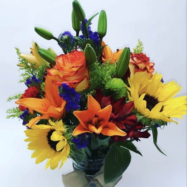Colorful bouquet with sunflowers, lilies, and roses in a glass vase