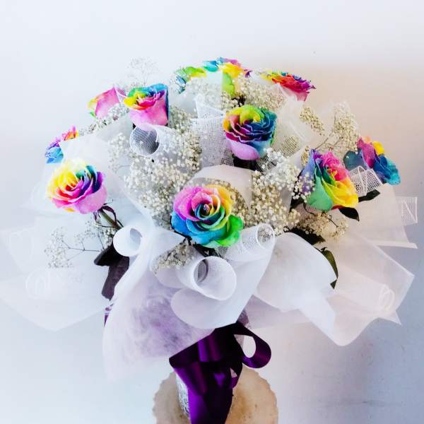Rainbow roses in white wrapping with baby's breath and a purple ribbon