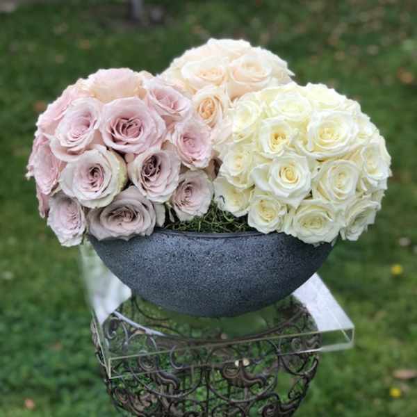 Three rose bouquets in pale pink, cream, and white arranged in a dark bowl