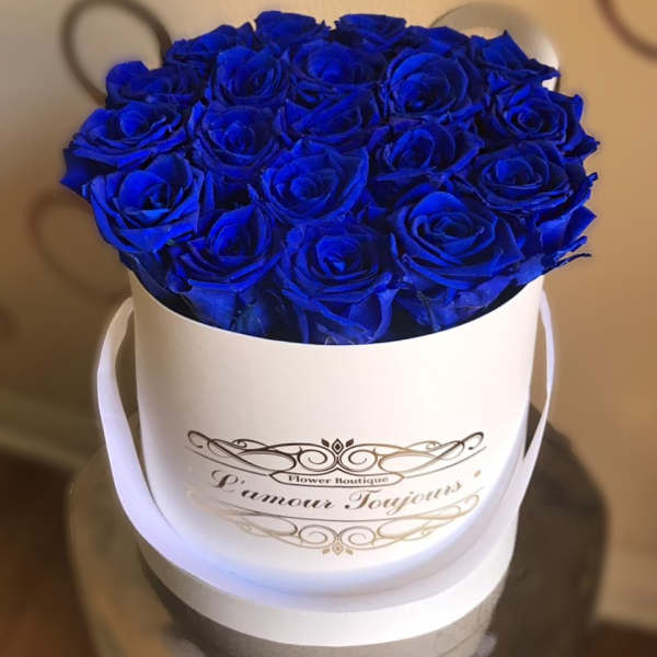 Blue roses arranged in a white round hatbox with ribbon handles