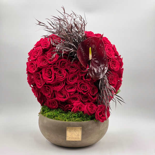 Round arrangement of red roses in a low bowl with a dark anthurium accent