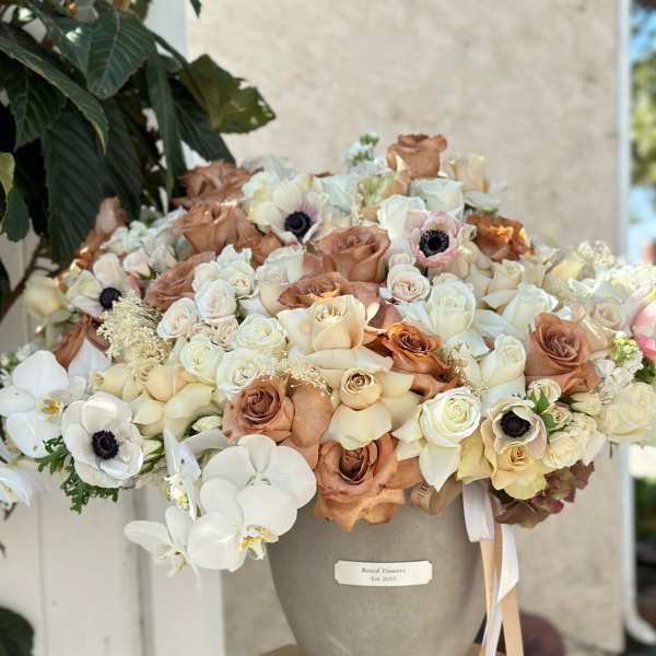 Large bouquet of cream and tan roses with white orchids in a gray vase