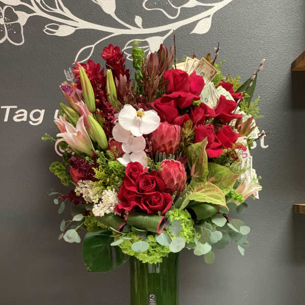 Tall red floral arrangement in a glass vase with a white orchid and dollar bills