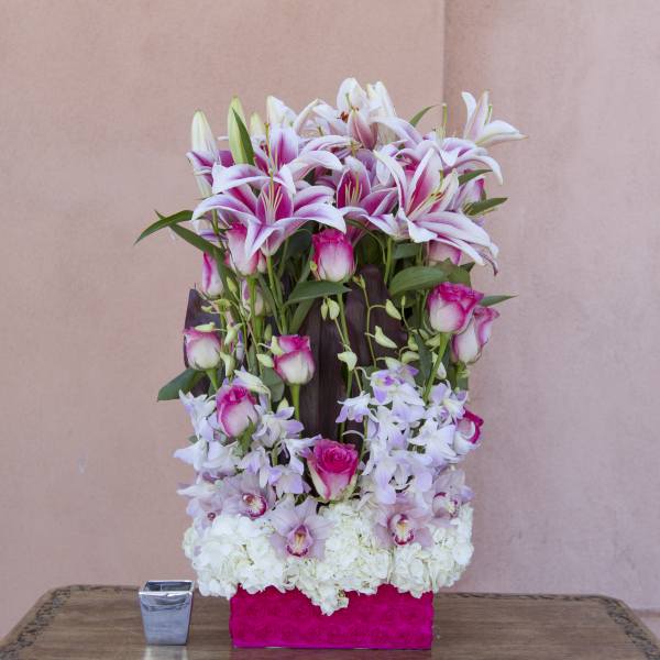 Tall floral arrangement with pink lilies, roses, orchids, and white hydrangeas in a pink box