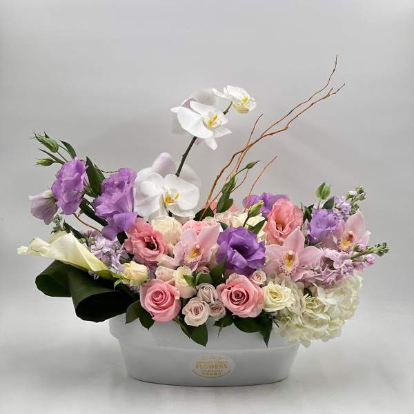 Pastel floral arrangement in a white container with orchids, roses, and hydrangea