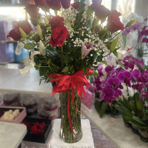 Tall bouquet of red roses and white lilies in a glass vase with a red ribbon