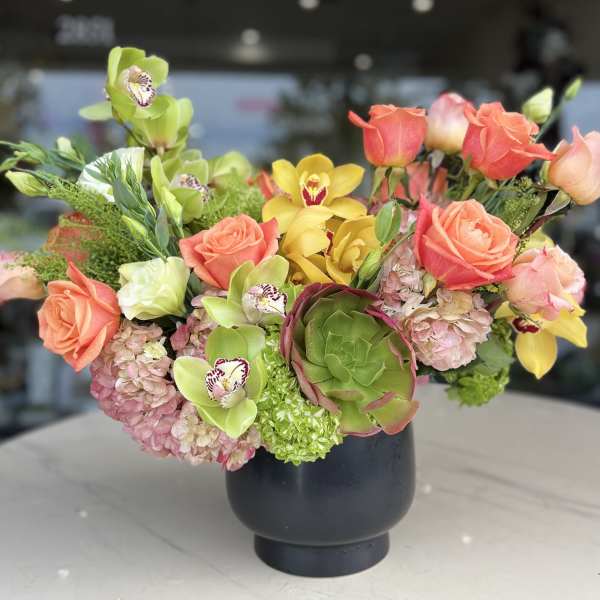Mixed bouquet with roses, orchids, hydrangeas, and a succulent in a black vase