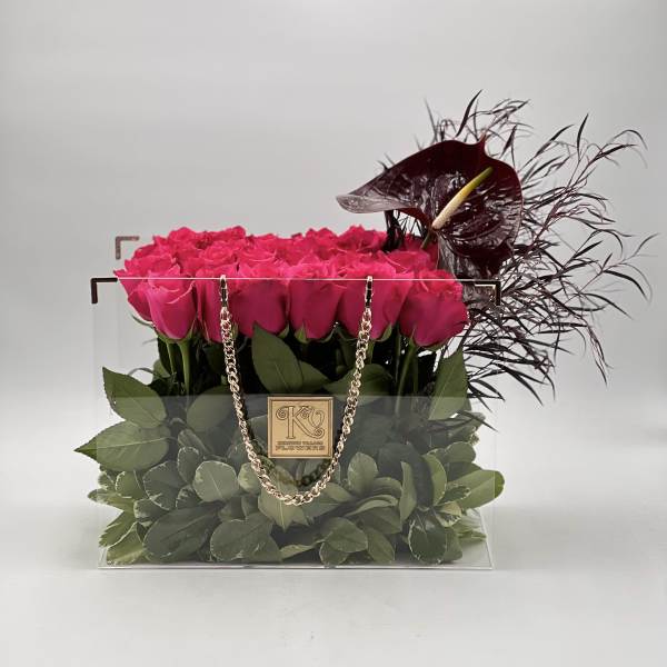 Pink roses in a clear square box with dark decorative flowers