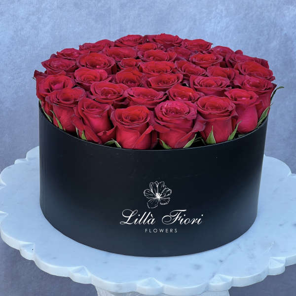 Round box filled with red roses on a white pedestal