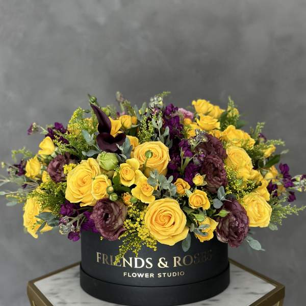 Yellow and purple roses arranged in a black round box