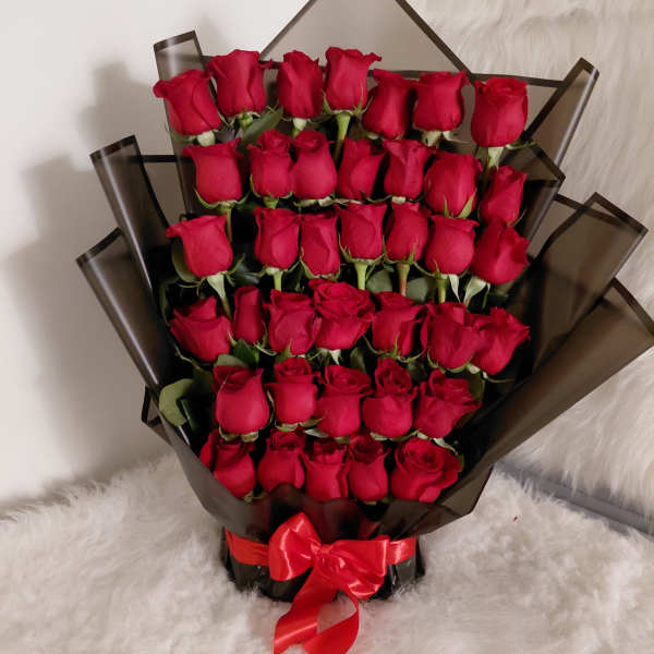 Large bouquet of red roses wrapped in dark paper with a red ribbon