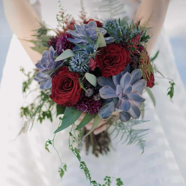 Bride holding a bouquet of red roses and blue-gray succulents