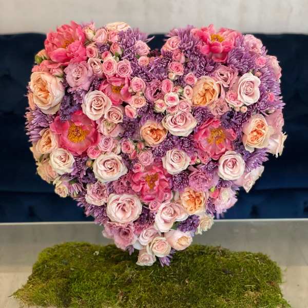 Heart-shaped bouquet of pink and purple flowers on a moss base