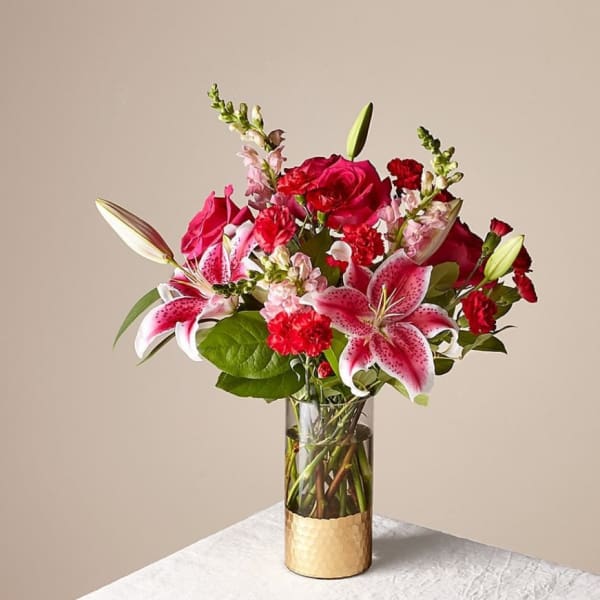 Bouquet of pink lilies, red roses, and carnations in a glass vase