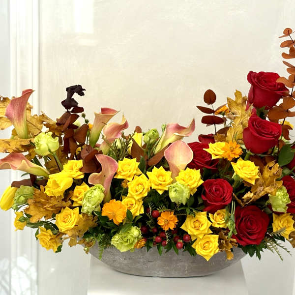 Autumn floral arrangement with red roses, yellow blooms, and calla lilies in a low bowl