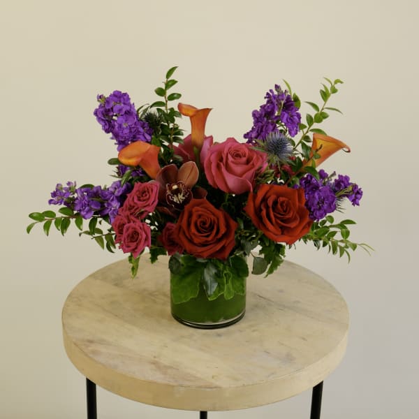 Mixed bouquet of roses, calla lilies, and purple flowers in a glass vase