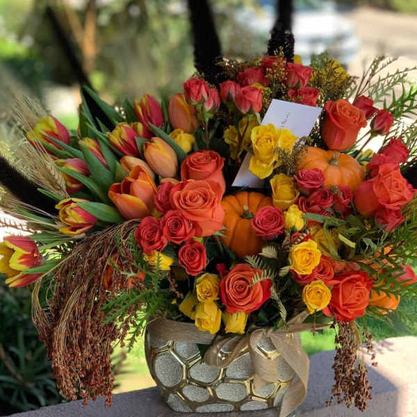 Mixed bouquet of roses and tulips in a decorative vase with pumpkins