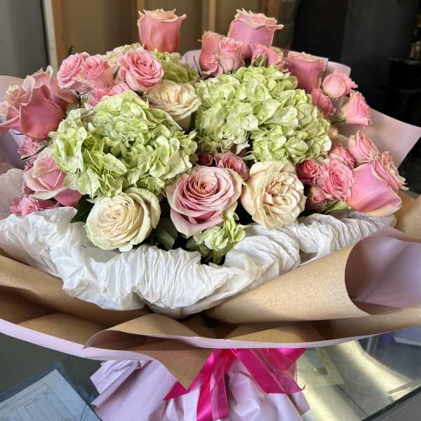 Bouquet of pink and cream roses with green hydrangeas wrapped in paper