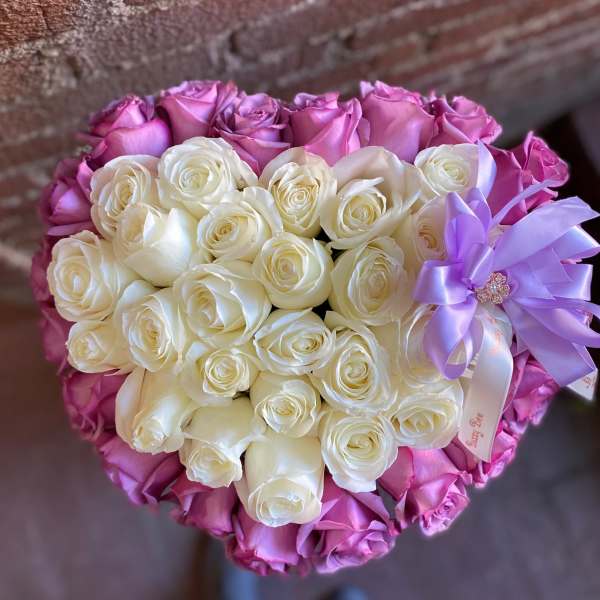 Heart-shaped arrangement of white and lavender roses with a lavender ribbon bow
