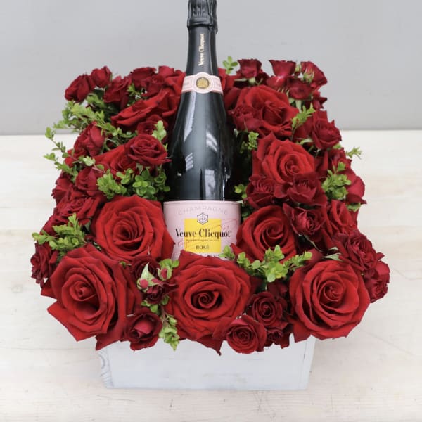 Red roses arranged around a champagne bottle in a white box