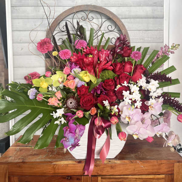 Large mixed floral arrangement in a white vase with pink, red, and white blooms