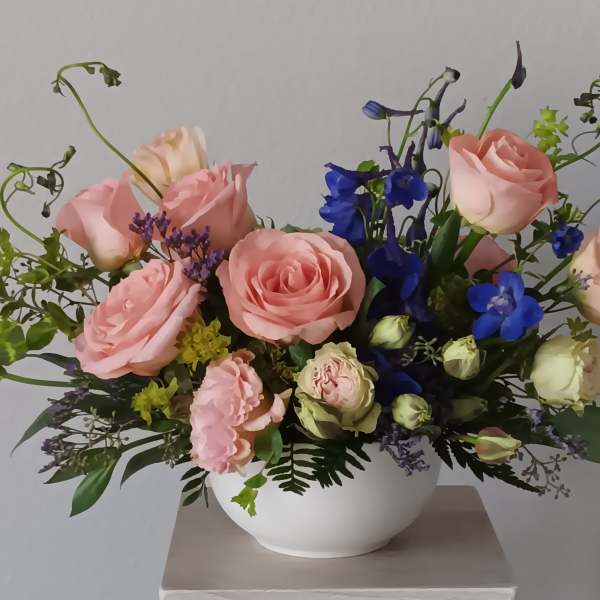 Pink roses and blue flowers arranged in a white bowl vase