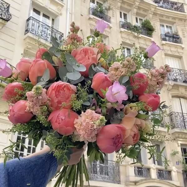 Large bouquet of pink peonies and pastel flowers held in front of a building