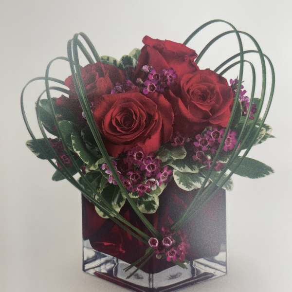 Red roses and purple filler flowers in a clear cube vase