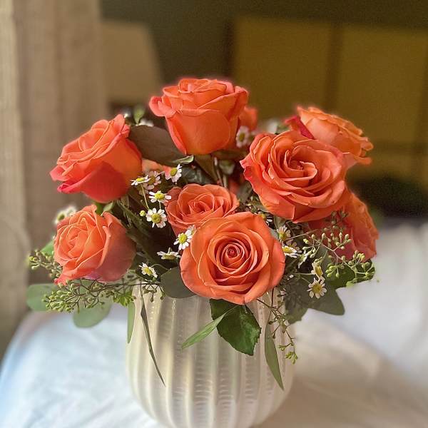 Orange roses arranged in a white ribbed vase