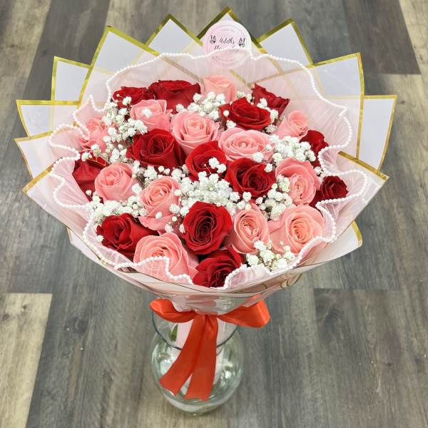 Bouquet of red and pink roses in pink wrap with a red ribbon, in a glass vase