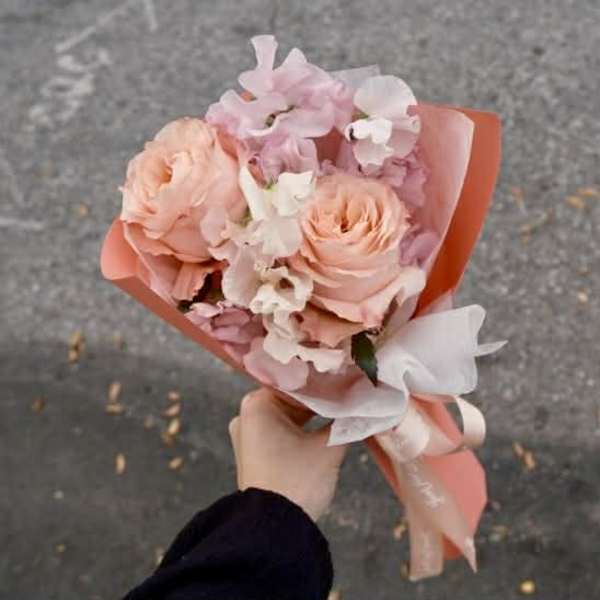 Handheld bouquet of peach and pink flowers wrapped in coral paper