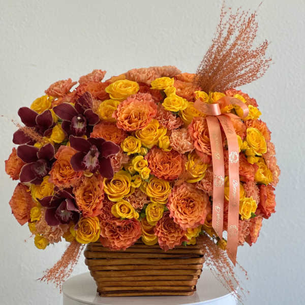 Orange and yellow floral arrangement in a woven basket with burgundy orchids