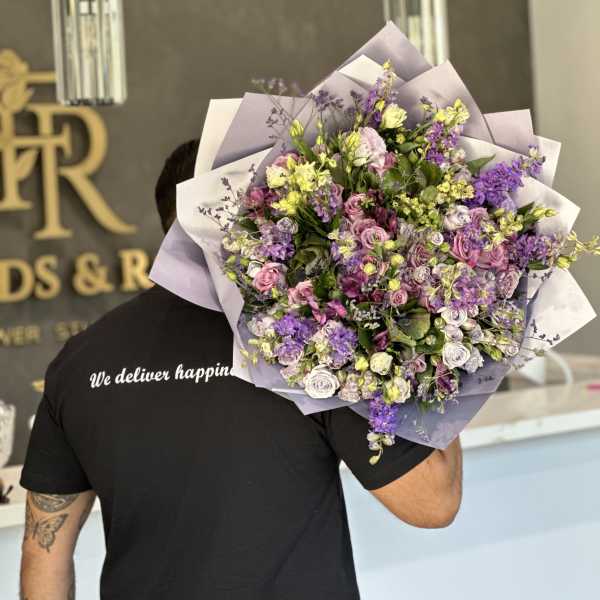 Large bouquet of purple, pink, and white flowers wrapped in lavender paper