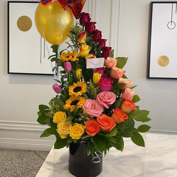 Tall bouquet of multicolored roses with balloons in a black vase