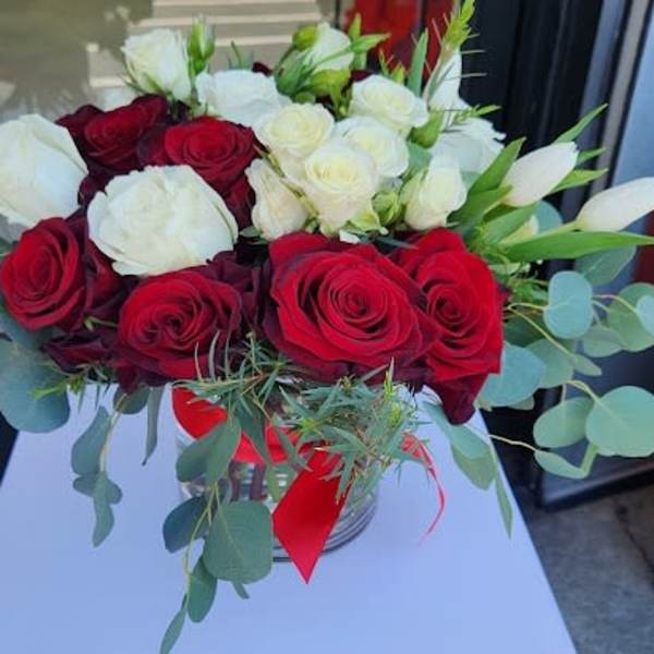 Low glass vase of red and white roses with white tulips and a red ribbon bow