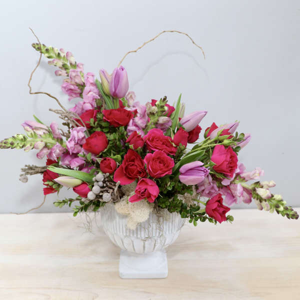 Low pink and red rose arrangement with tulips in a white pedestal bowl